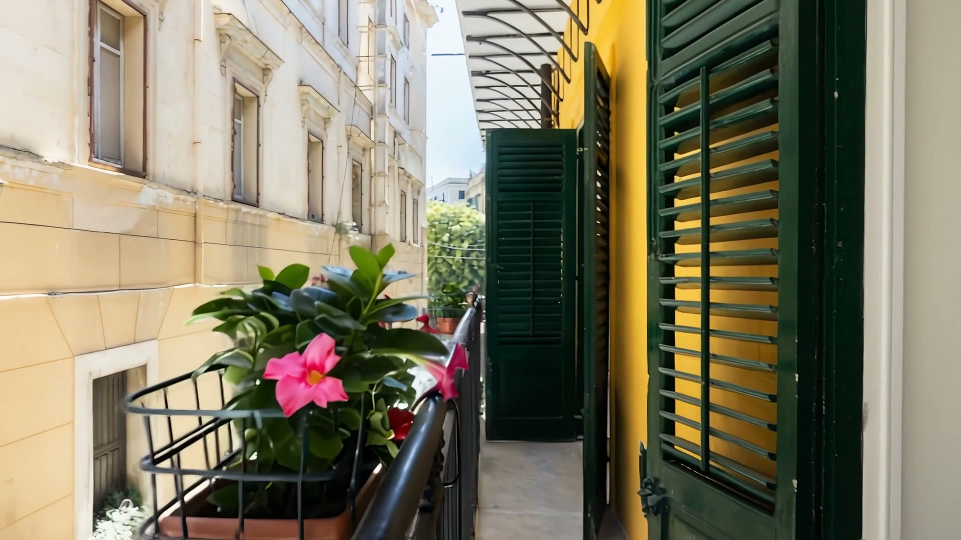Il balcone con le persiane verdi e una dipladenia rosa